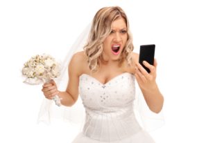 Furious young bride looking at her cell phone and screaming isolated on white background